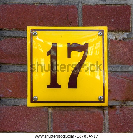 Enameled house number seventeen. Brown lettering on a yellow background.