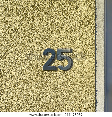 metal house number twenty five. Separate lettering on a yellow stucco wall.