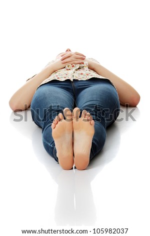 Young woman wearing blue jeans and flower top is lying on her back on the floor with her hands crossed on belly. Relaxed woman showing soles of her bare feet. Isolated on the white background.