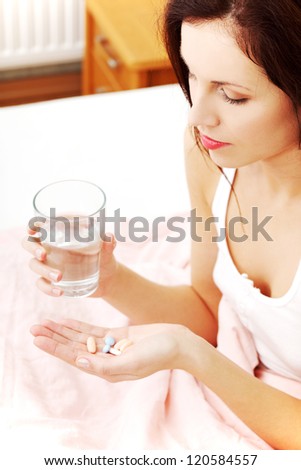 Beautiful woman at bed taking pills.