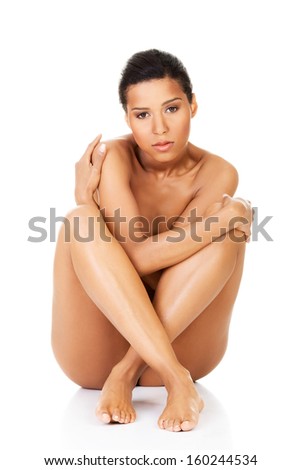 Beautiful and naked women sitting and covering her nudity by her legs and arms. Front view. . Isolated on white.