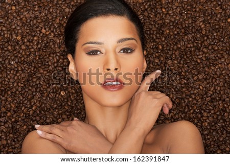 Attractive woman lying in coffee grains. Fron view. Closeup.