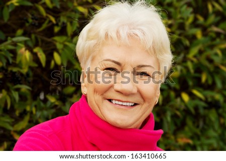 Portrait of a cheerful old lady over green background. Outdoor.