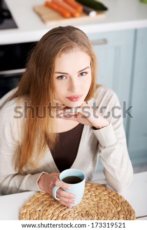 Beautiful caucasian woman is sitting by table with cup of coffee. Indoor background.
