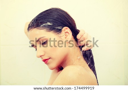 Beautiful young woman washing her hairs in a shower