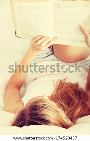 Beautiful young blond woman reading book on the bed at home