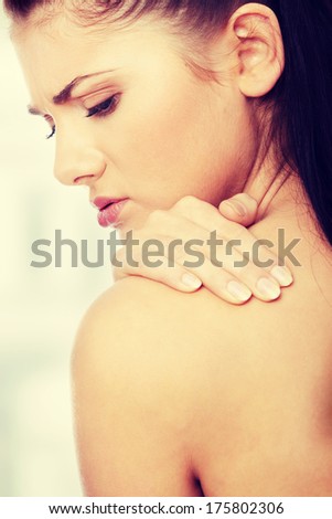 Woman from behind, naked body, holding her neck on the left side. Vertical.