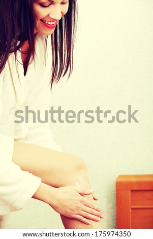 Groomed woman dressed in a dressing-gown, lubricating her leg in the bedroom.