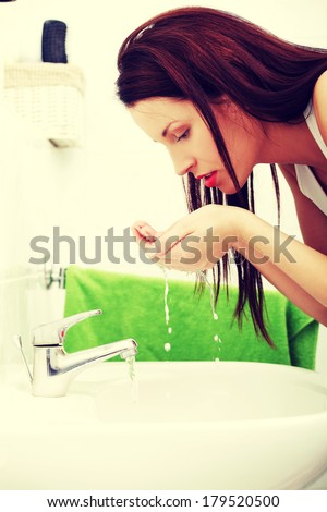 Site view of a young groomed woman washing her face in the bathroom in the morning - green towel in the background.