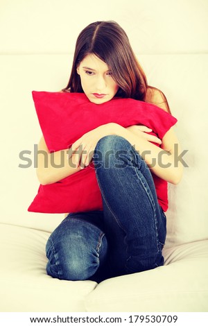 Sad woman\'s sitting on couch and squeezeing pillow.