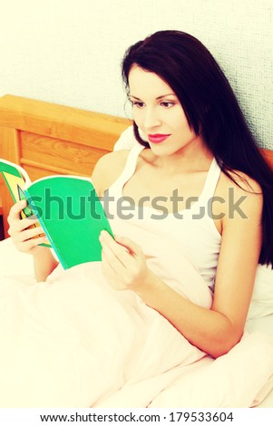Portrait of a young beautiful relaxed woman reading a book in bed in the morning.