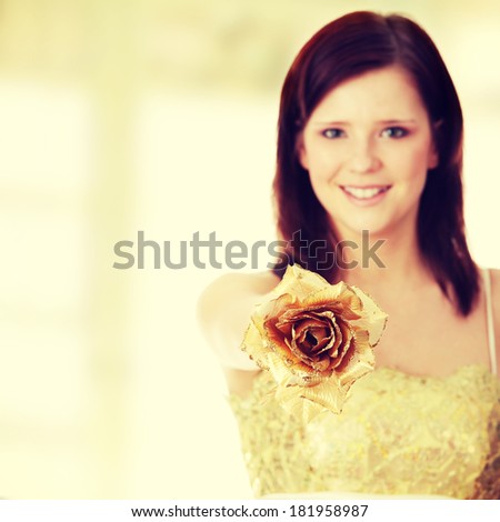 Young beautiful woman in elegant, evening, gold dress, holding gold rose. Focus on rose