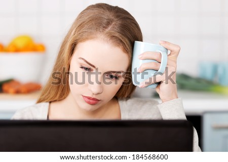 Beautiful caucasian woman sitting with hot drink and working on laptop. Indoor background.