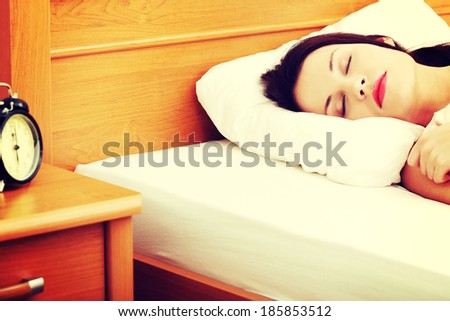 Face closeup of a young beautiful woman sleeping in bed, with a black alarm clock in the left site of the picture.