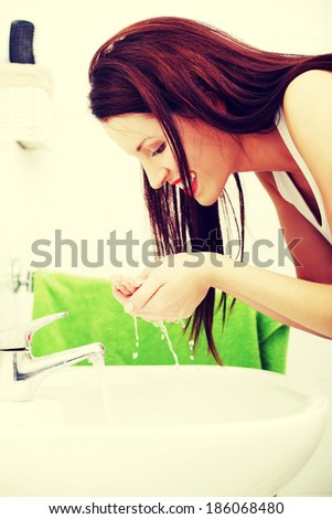 Site view of a young smiling woman washing her face in the bathroom in the morning - green towel in the background.