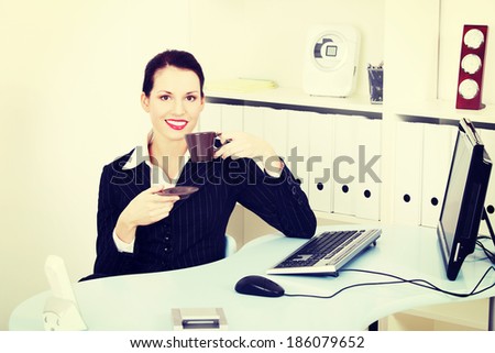 Pretty smiling businesswoman drinking coffee in the office.