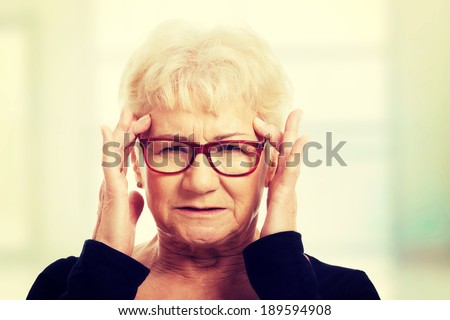 An old woman is eye glasses is having a headache.