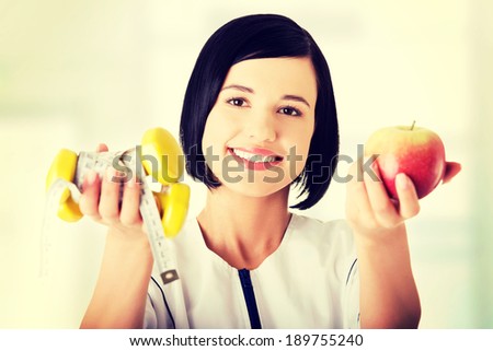 Woman dietician holding apple and dumbbells with measuring tape