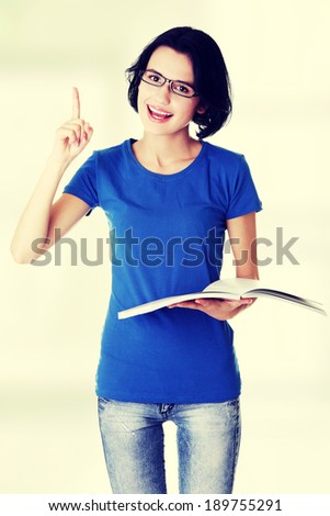 Studying happy young woman reading her notebook for school and pointing on copy space.