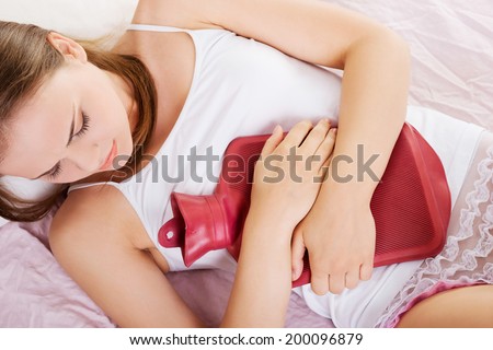 Woman lying in bed with hot water bag and holding it on her belly.