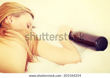 Drunk zoung topless woman sleeping on bed with bottle of vine in hand. Isolated on white