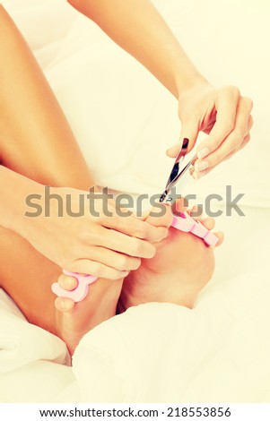 Attractive young woman cutting her feat nails in bed