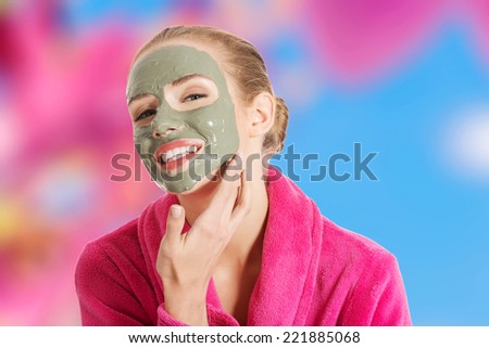 Beautiful woman in pink bathrobe and havinf facial mask.