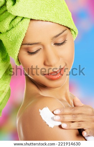 Attractive woman rubbing a body lotion on her arm. Side view. Wrapped in towel with turban.