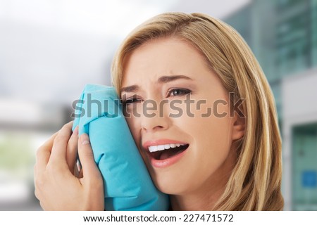Woman having tooth ache holding ice bag near face