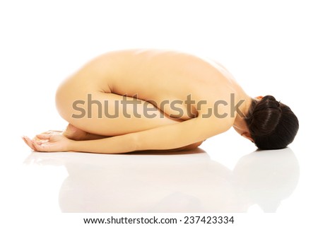 Nude depressed woman curled up on the floor.
