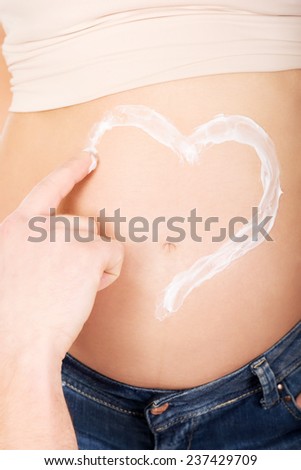Man applying a cream with heart shape on wife\'s belly