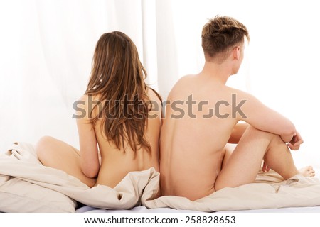 Young depressed naked couple sitting on bed.