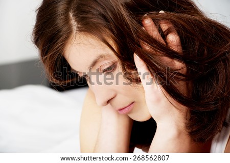 Sad depressed woman sitting on bed.