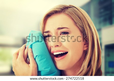 Woman having tooth ache holding ice bag near face