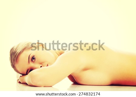Side view of a nude woman lying on hands on the floor with folded hands, looking at the camera