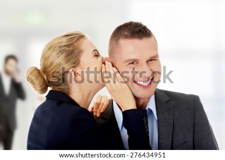 Businesswoman whispers gossip to businessman.
