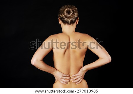 Back view of naked woman touching her back.