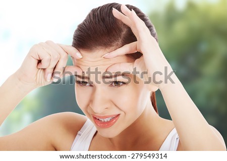 Shocked young woman checking wrinkles on forehead.