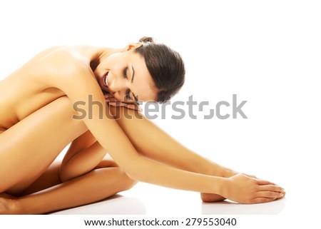 Side view of naked slim woman sitting curled up, embracing leg