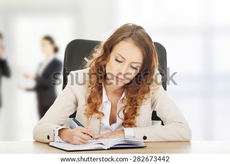 Focused businesswoman writing note by a desk.