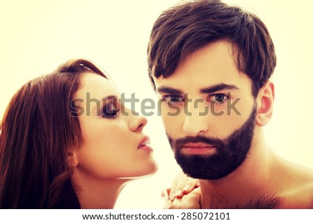 Beautiful topless woman whispering to shirtless man\'s ear.