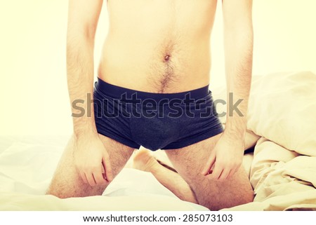 Shirtless man sitting on knees in bed.