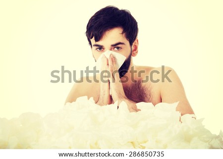 Sick man with a lot of tissues sneezing into handkerchief.