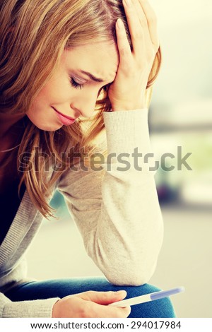Sad young woman holding pregnancy test.