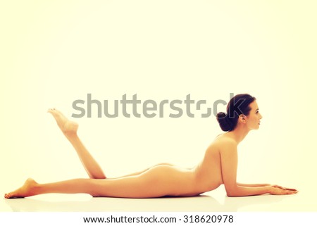 Slim nude woman lying on belly holding legs up