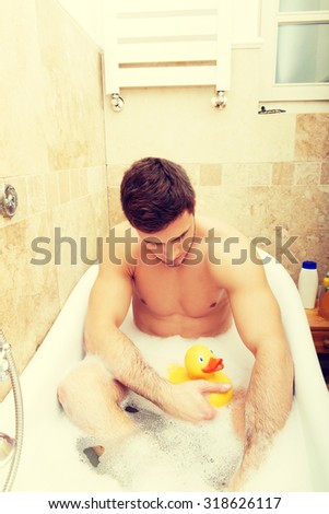 Handsome man taking a bath with duck toy and enjoying it.