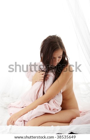 Yong brunette sitting on the bed and covering her naked body with pink bed sheet