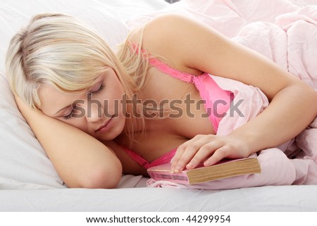 Sensual young woman laying in pink bed. Reading