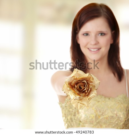 Young beautiful woman in elegant, evening, gold dress, holding gold rose isolated on white background. Focus on rose
