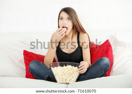 Beautiful young woman watching TV and eating popcorn